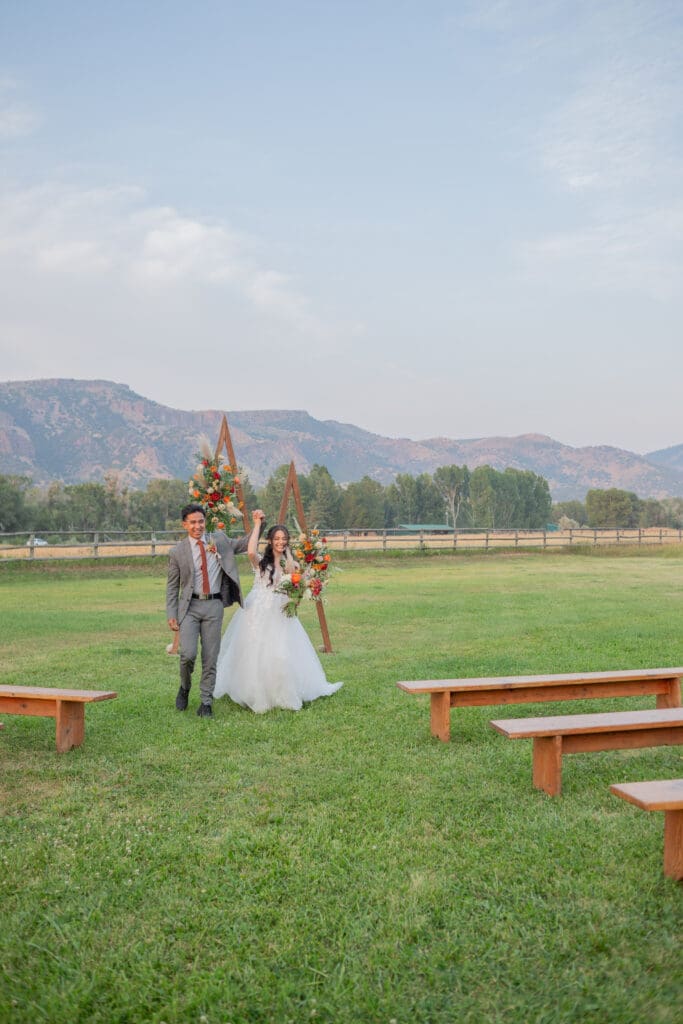 bride-and-groom-holding-hands-walking-back-down-the-aisle-after-getting-married-with-mountain-backdrop-captured-by-snohomish-wedding-photographer