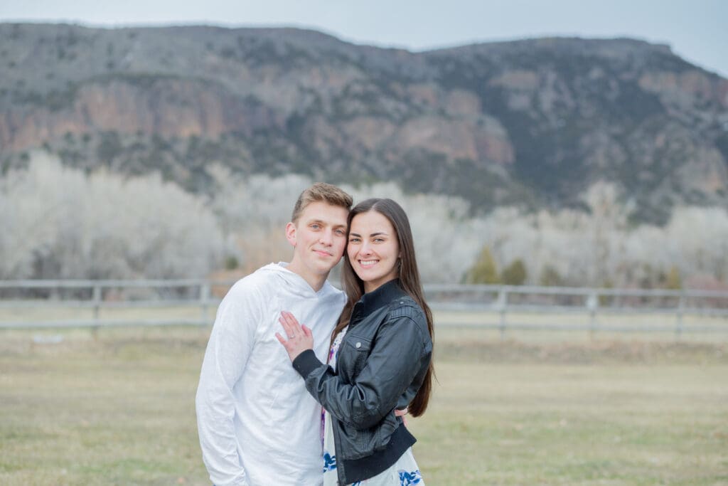 engaged-couple-looking-at-camera-with-mountain-backdrop