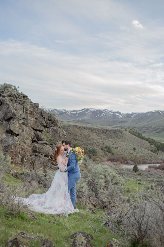 Wedding couple with bride in floral dress and groom in blue suit captured by a Seattle Wedding Photographer with a mountain backdrop