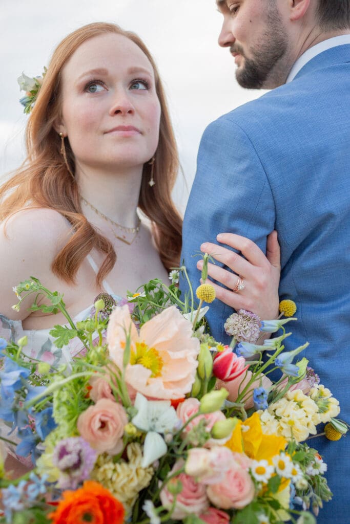 Seattle Wedding Photographer captures bride looking off in the distance while holding a bridal bouquet and wrapped around grooms arm